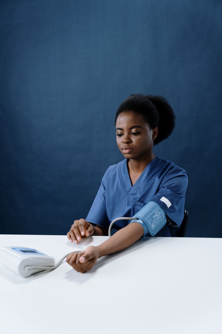 A nurse in navy scrubs taking a blood pressure reading at a table